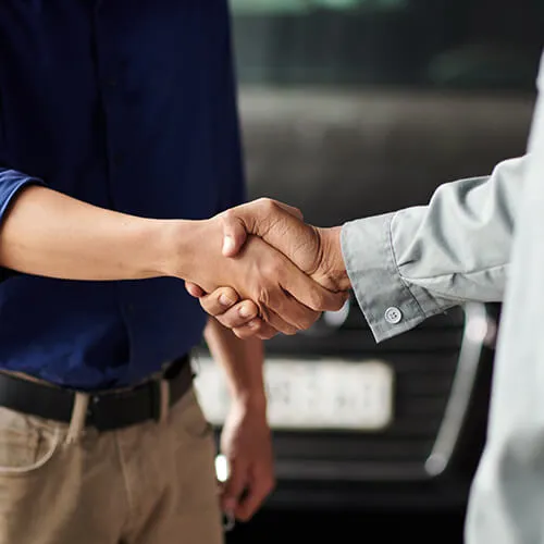 Two people shaking hands near car.